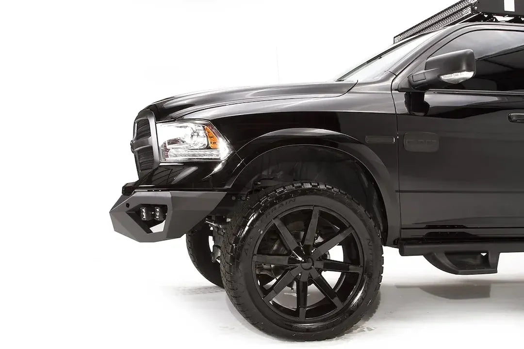 Fab Fours Vengeance front bumper on a black Ram 1500, driver-side profile view, showing the bumper wing depth, cube light pod, and tire clearance