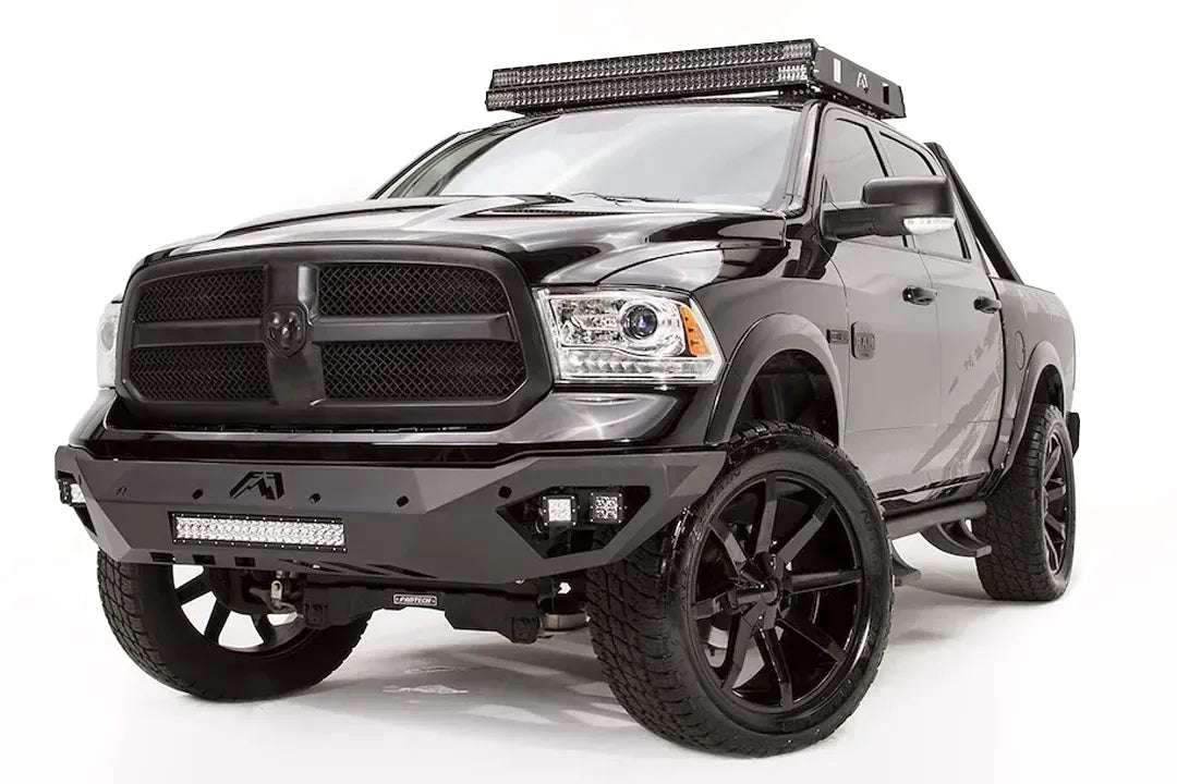 Fab Fours Vengeance front bumper on a black Ram 1500, front passenger-side three-quarter view, showing the LED light bar, cube lights, and angular bumper wing
