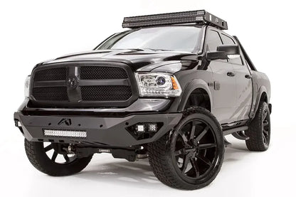 Fab Fours Vengeance front bumper on a black Ram 1500, front passenger-side three-quarter view, showing the LED light bar, cube lights, and angular bumper wing