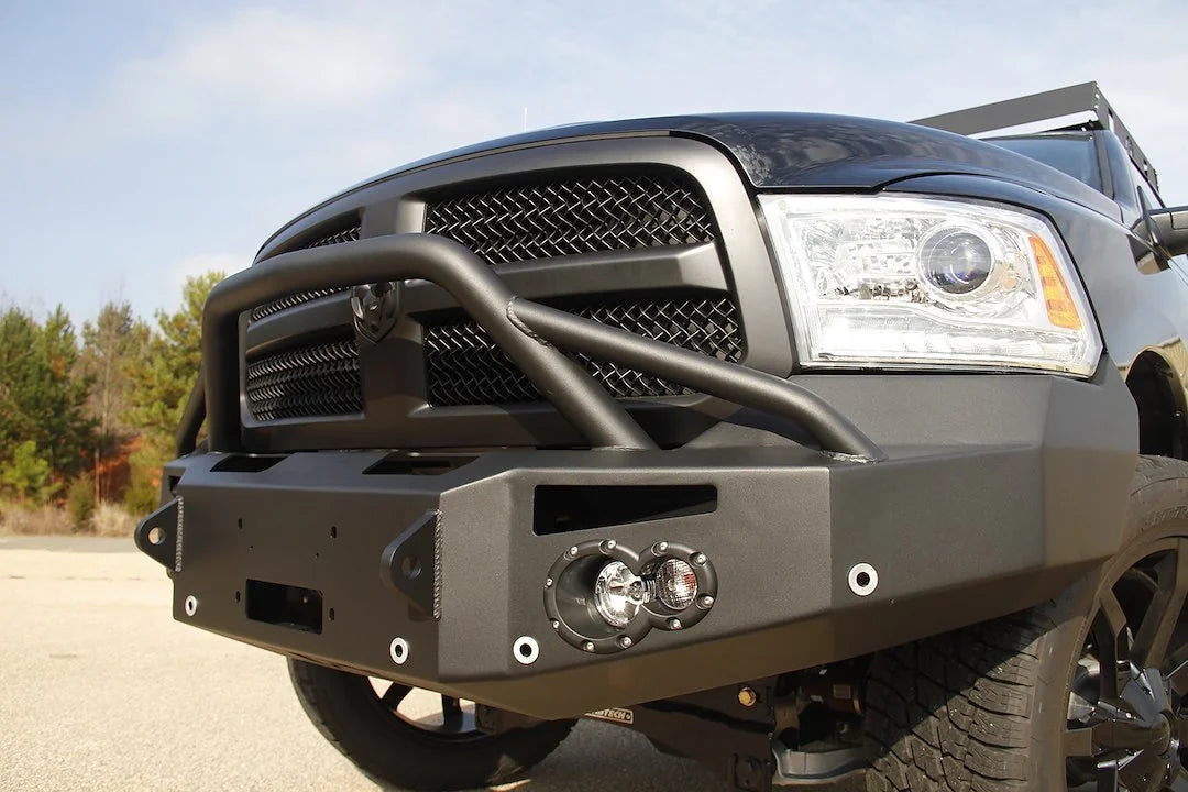 Fab Fours Premium front bumper with pre-runner guard on a black Ram 1500, low close-up of the front corner outdoors, showing the pre-runner tube, round light pod and bumper end cap