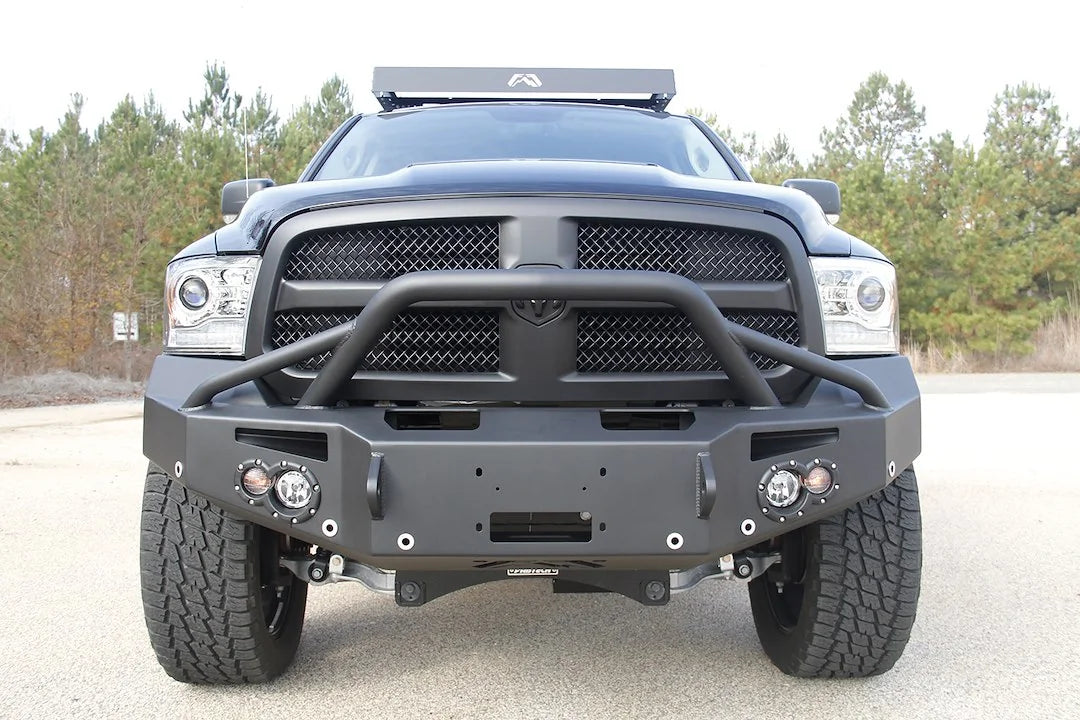 Fab Fours Premium front bumper with pre-runner guard on a black Ram 1500, straight-on front view outdoors, showing the pre-runner hoop, winch fairlead opening, round lights and D-ring mounts