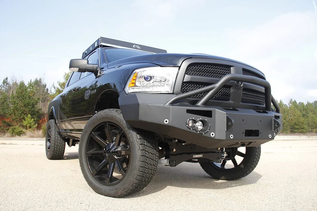 Fab Fours Premium front bumper with pre-runner guard on a black Ram 1500, front passenger-side three-quarter view outdoors, showing the pre-runner hoop, round lights and winch mount