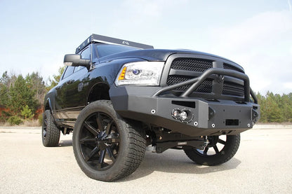 Fab Fours Premium front bumper with pre-runner guard on a black Ram 1500, front passenger-side three-quarter view outdoors, showing the pre-runner hoop, round lights and winch mount
