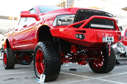 Fab Fours Premium front bumper with pre-runner guard in red on a red lifted Ram 1500, front passenger-side view outdoors, showing the pre-runner hoop, winch and round lights