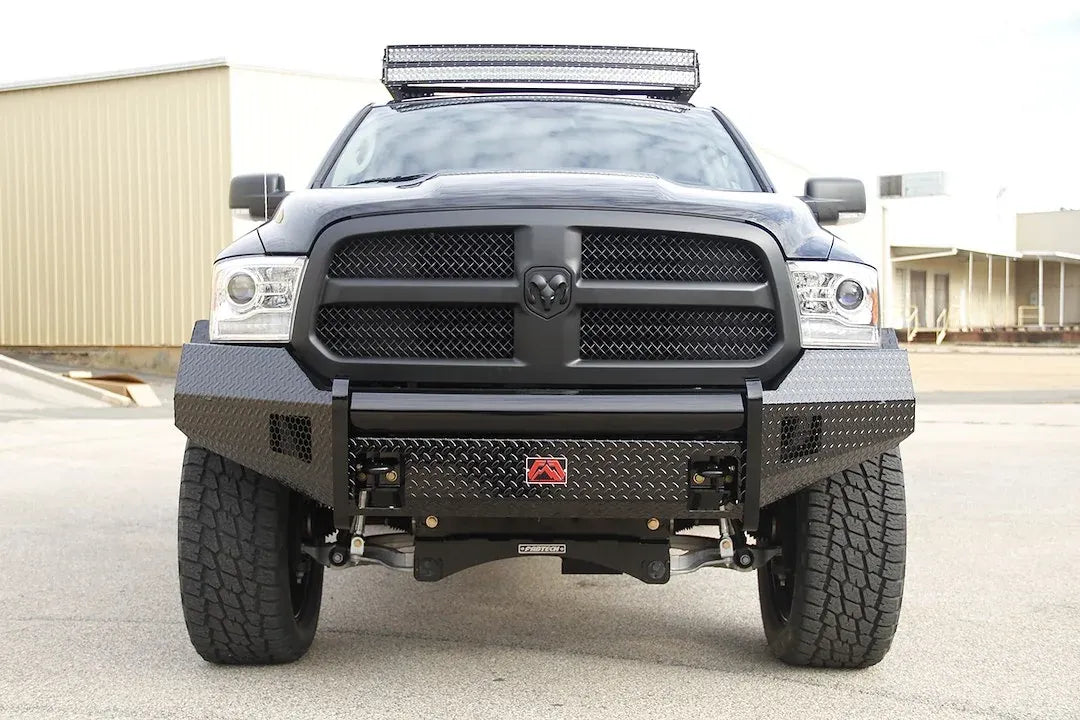 Fab Fours Black Steel front bumper on a black Ram 1500, straight-on front view outdoors, showing the diamond-plate face, center tube and red logo badge