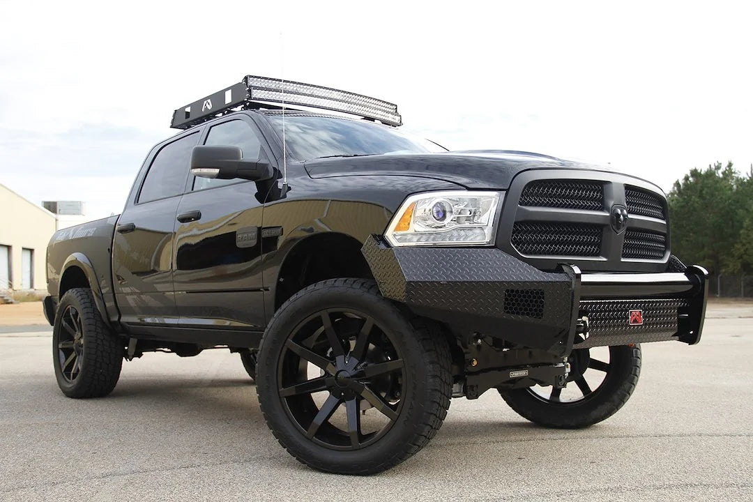 Fab Fours Black Steel front bumper on a black Ram 1500, front passenger-side three-quarter view outdoors, showing the diamond-plate face, wrap-around wings and center tube