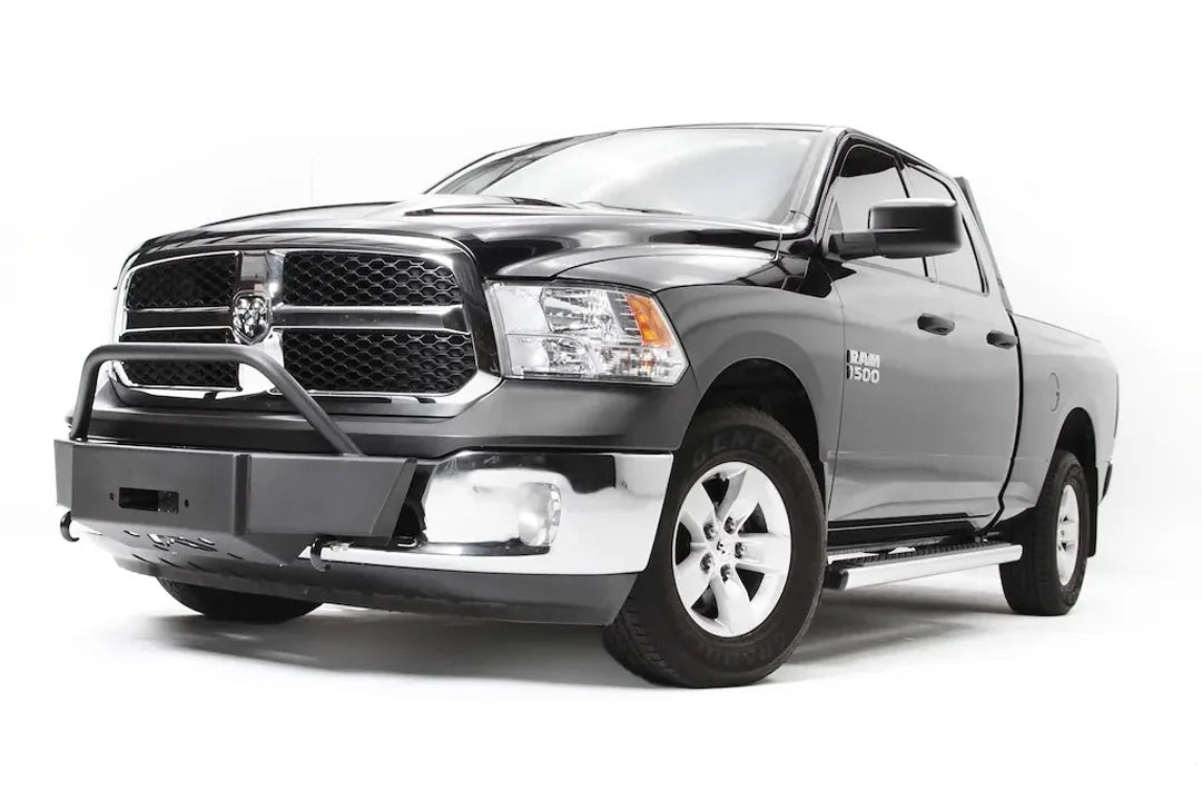 Fab Fours winch mount on a dark gray Ram 1500, front driver-side three-quarter view, showing the low-profile winch plate, tube hoop and retained factory bumper ends