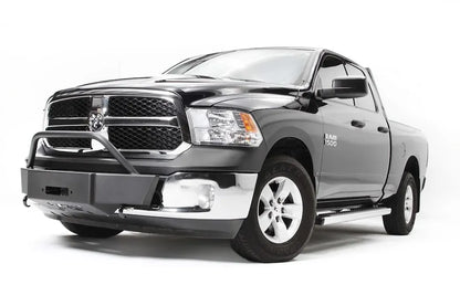 Fab Fours winch mount on a dark gray Ram 1500, front driver-side three-quarter view, showing the low-profile winch plate, tube hoop and retained factory bumper ends