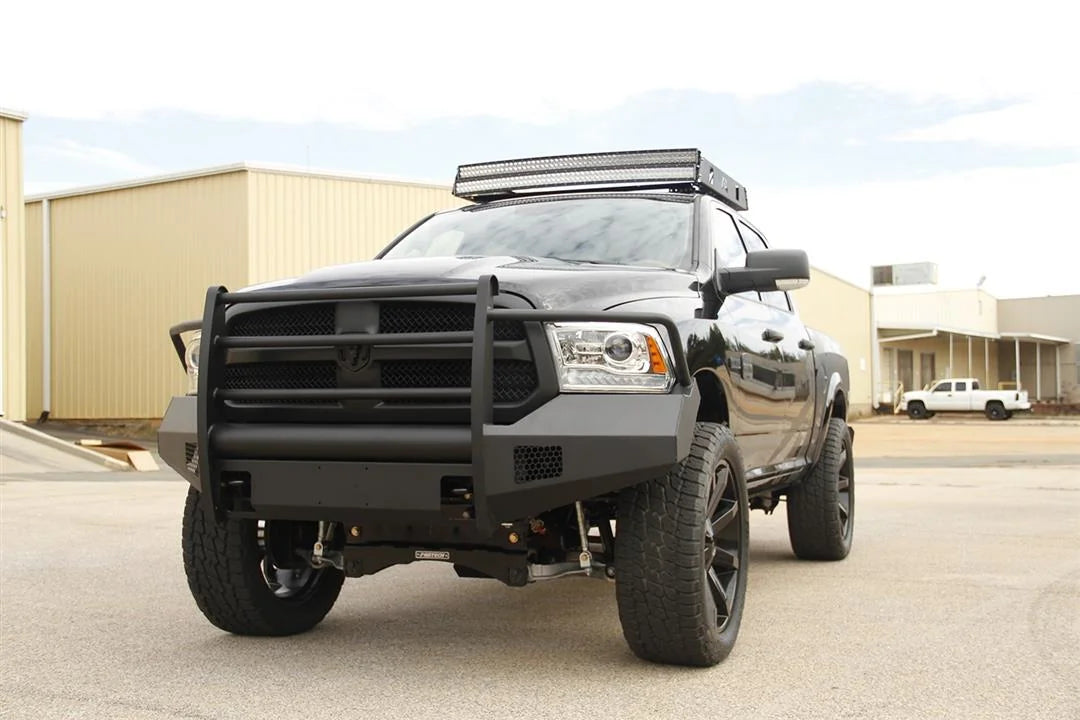 Fab Fours Black Steel Elite front bumper with full guard on a black Ram 1500, front driver-side three-quarter view outdoors, showing the full grille guard uprights, wrap-around wings and mesh inserts