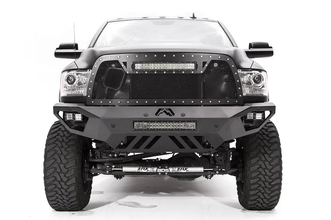 Fab Fours Vengeance front bumper on a dark gray lifted Ram 2500, straight-on front view, showing the integrated light bar, cube light pods and slotted skid plate