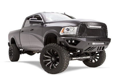 Fab Fours Vengeance front bumper on a dark gray lifted Ram 2500, front passenger-side three-quarter view, showing the integrated light bar, cube light pods and skid plate