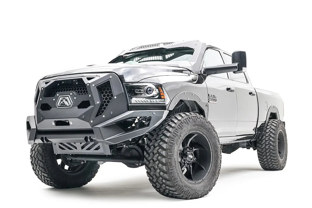 Fab Fours front bumper on a silver lifted Ram 2500, front driver-side three-quarter view, showing the mesh grille guard panel, winch opening and skid plate