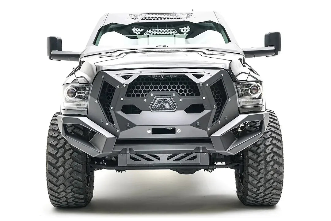 Fab Fours front bumper on a silver lifted Ram 2500, straight-on front view, showing the mesh grille guard panel, winch opening and skid plate