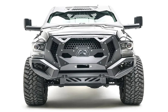 Fab Fours front bumper on a silver lifted Ram 2500, straight-on front view, showing the mesh grille guard panel, winch opening and skid plate