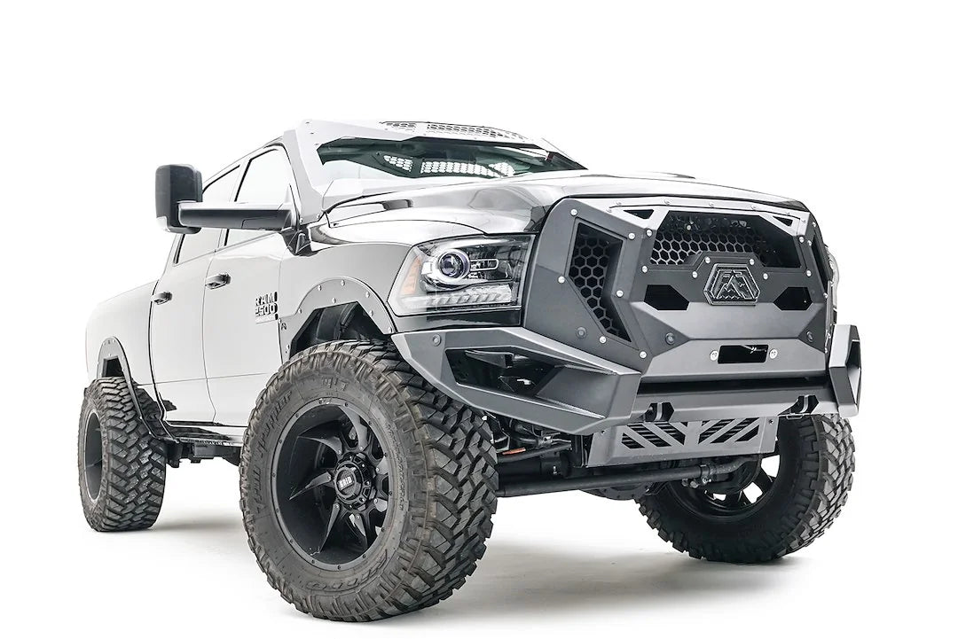 Fab Fours front bumper on a silver lifted Ram 2500, front passenger-side three-quarter view, showing the mesh grille guard panel, bumper wing and skid plate