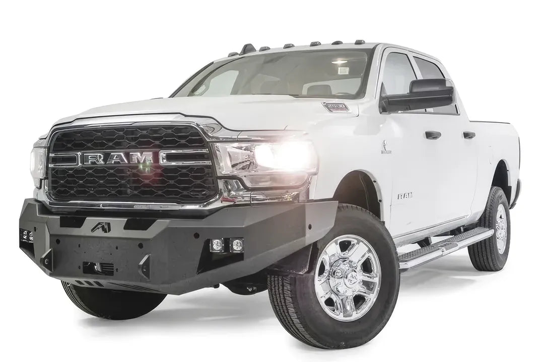 Fab Fours Premium winch bumper on a white Ram 2500, front driver-side three-quarter view, showing the winch mount, cube light pods and angled bumper ends