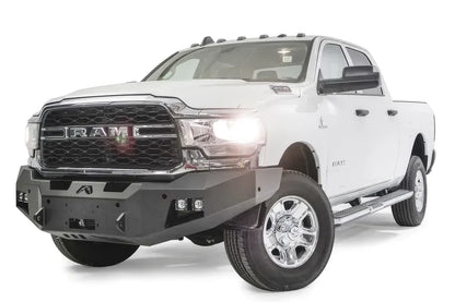 Fab Fours Premium winch bumper on a white Ram 2500, front driver-side three-quarter view, showing the winch mount, cube light pods and angled bumper ends