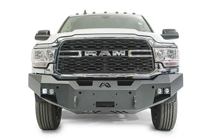 Fab Fours Premium winch bumper on a white Ram 2500, straight-on front view, showing the winch fairlead opening, cube light pods and skid plate