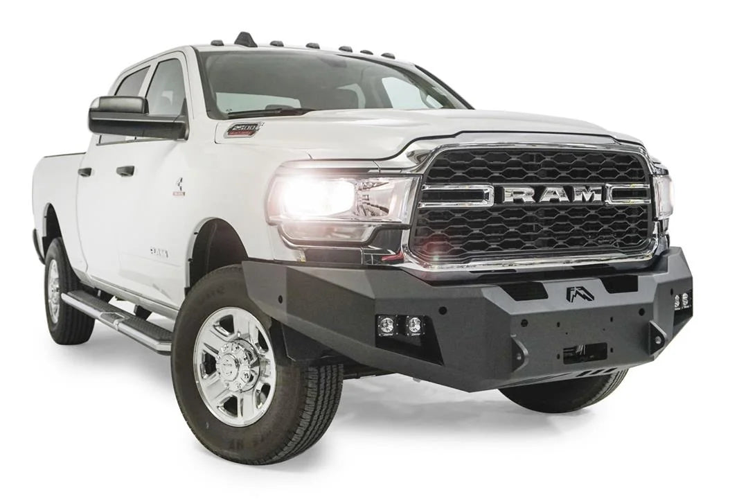 Fab Fours Premium winch bumper on a white Ram 2500, front passenger-side three-quarter view, showing the winch mount, cube light pods and angled bumper ends