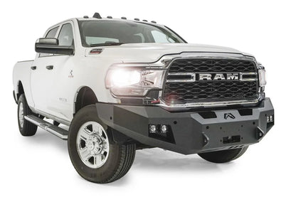 Fab Fours Premium winch bumper on a white Ram 2500, front passenger-side three-quarter view, showing the winch mount, cube light pods and angled bumper ends