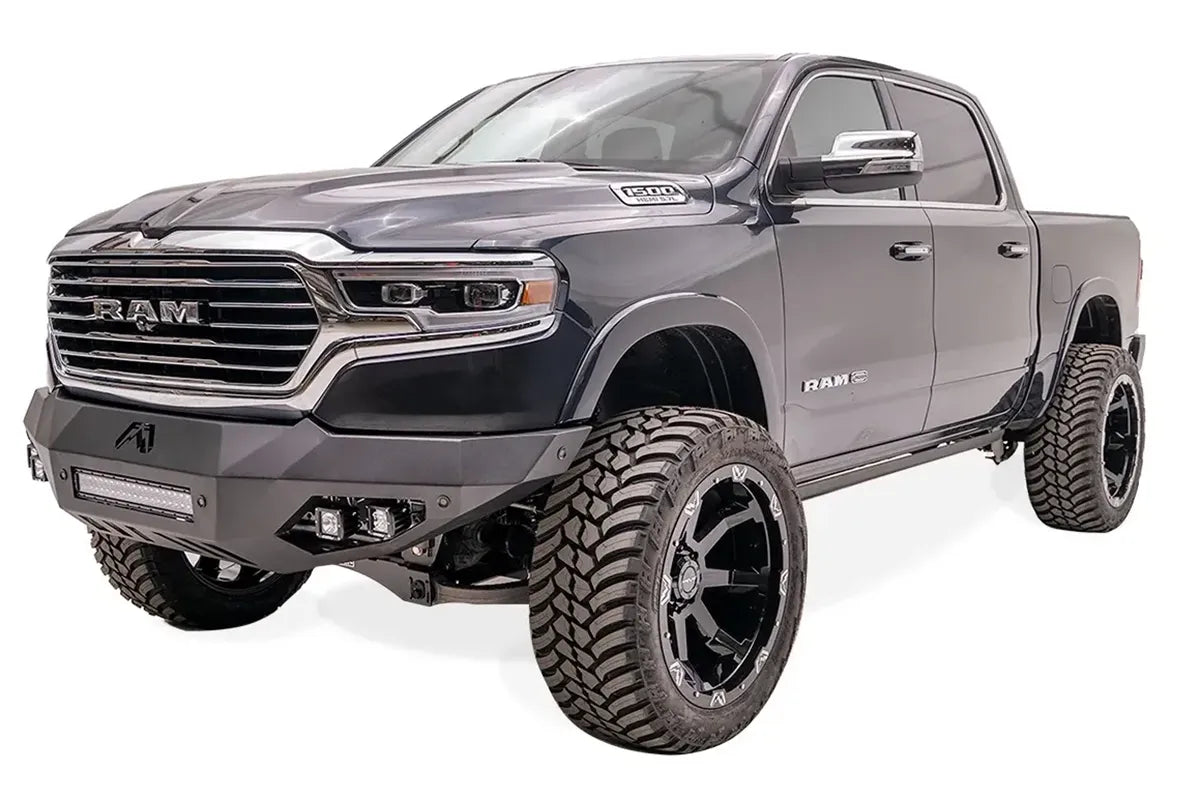 Fab Fours Vengeance front bumper on a dark blue lifted Ram 1500, front driver-side three-quarter view, showing the integrated light bar, cube lights and angled wings