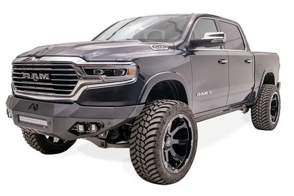Fab Fours Vengeance front bumper on a dark blue lifted Ram 1500, front driver-side three-quarter view, showing the integrated light bar, cube lights and angled wings
