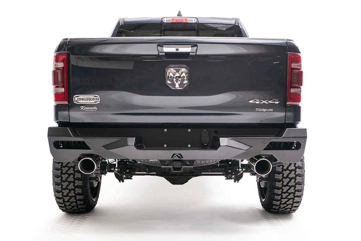 Fab Fours Vengeance rear bumper on a lifted dark gray Ram 1500, straight rear view, with honeycomb mesh light openings, center license plate area, hitch receiver, and dual exhaust tips