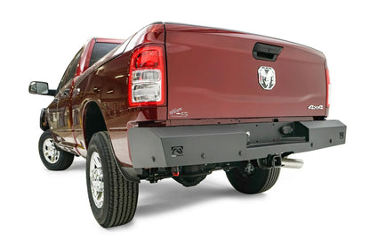 Fab Fours Red Steel rear bumper on a dark red Ram 2500, rear driver-side three-quarter view, showing the bumper wrap, logo end cutout and receiver hitch access