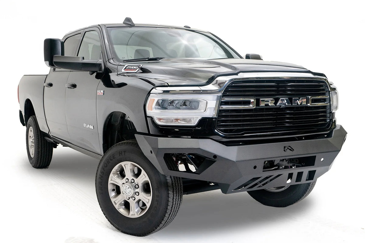 Fab Fours Vengeance front bumper on a black Ram 2500, front passenger-side three-quarter view, showing the angled wings, center logo and slotted skid plate