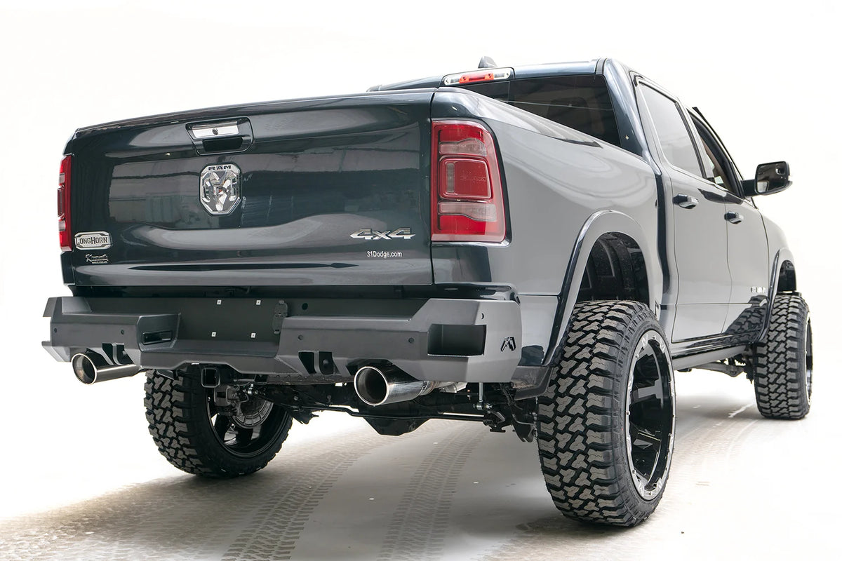 Fab Fours Premium rear bumper on a dark gray lifted Ram 1500, rear passenger-side three-quarter view, showing the dual exhaust cutouts, sensor ports and wrap-around end