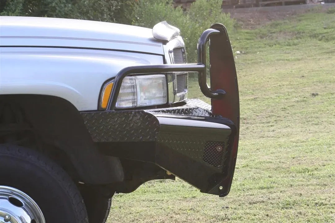 Fab Fours Black Steel front ranch bumper with full guard on a silver Ram 2500, close-up of the passenger-side bumper corner outdoors, showing the guard upright, diamond-plate wing and tubular hoop