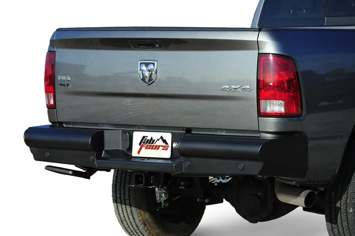 Fab Fours Black Steel Elite rear bumper on a gray Ram 2500, close-up rear view on a white background, showing the smooth bumper face, center plate pocket and hitch receiver