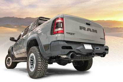 Fab Fours Vengeance rear bumper on a gray Ram 1500 TRX with sport bar, driver-side rear three-quarter view with desert sunset background, with parking sensors and hitch receiver