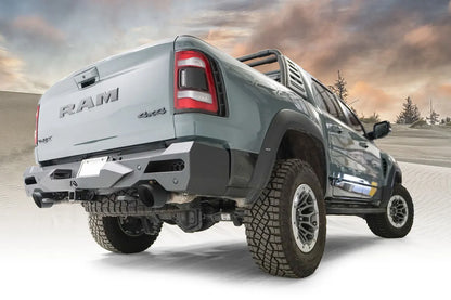 Fab Fours Vengeance rear bumper on a gray Ram 1500 TRX with sport bar, low passenger-side rear three-quarter view with desert dune background, with parking sensors and hitch receiver
