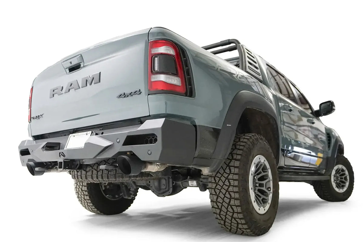 Fab Fours Vengeance rear bumper on a gray Ram 1500 TRX with sport bar, low passenger-side rear three-quarter view, with parking sensors, hitch receiver, and dual black exhaust tips