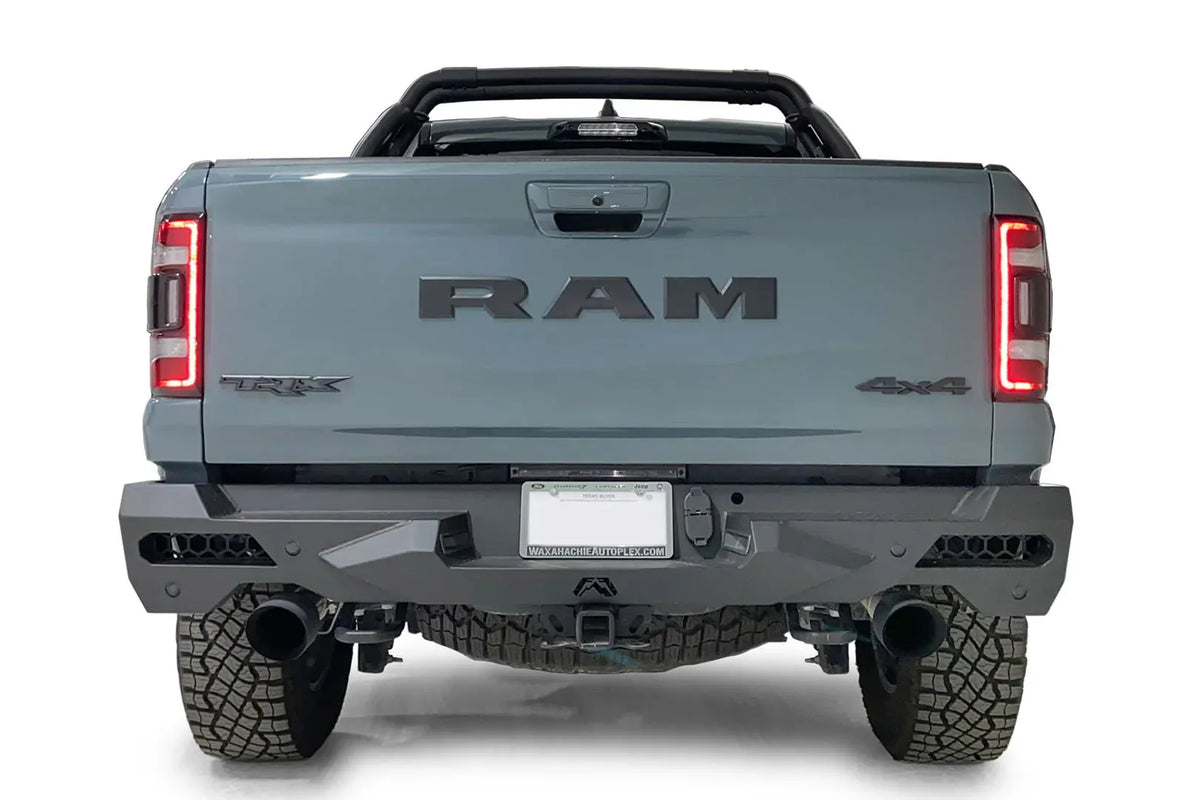 Fab Fours Vengeance rear bumper on a gray Ram 1500 TRX, straight rear view, with honeycomb mesh light openings, center license plate mount, hitch receiver, and dual black exhaust tips