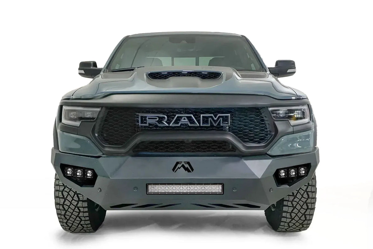 Fab Fours Vengeance front bumper on a gray Ram 1500 TRX, straight-on front studio view, showing the sculpted bumper face, center light bar and cube light pods