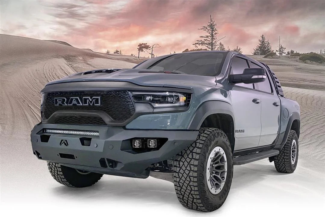 Fab Fours Matrix front bumper on a gray Ram 1500 TRX, front driver-side three-quarter view against a dune backdrop, showing the full-width bumper, top light bar and cube light pods