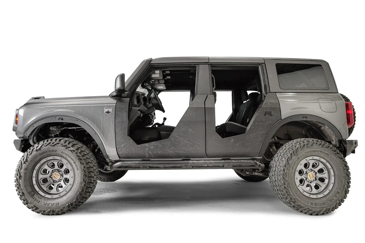 Fab Fours Trail Doors on a gray four-door Ford Bronco, driver-side profile, showing trail scratches on the matte black steel doors after off-road use