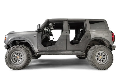 Fab Fours Trail Doors on a gray four-door Ford Bronco, driver-side profile, showing trail scratches on the matte black steel doors after off-road use