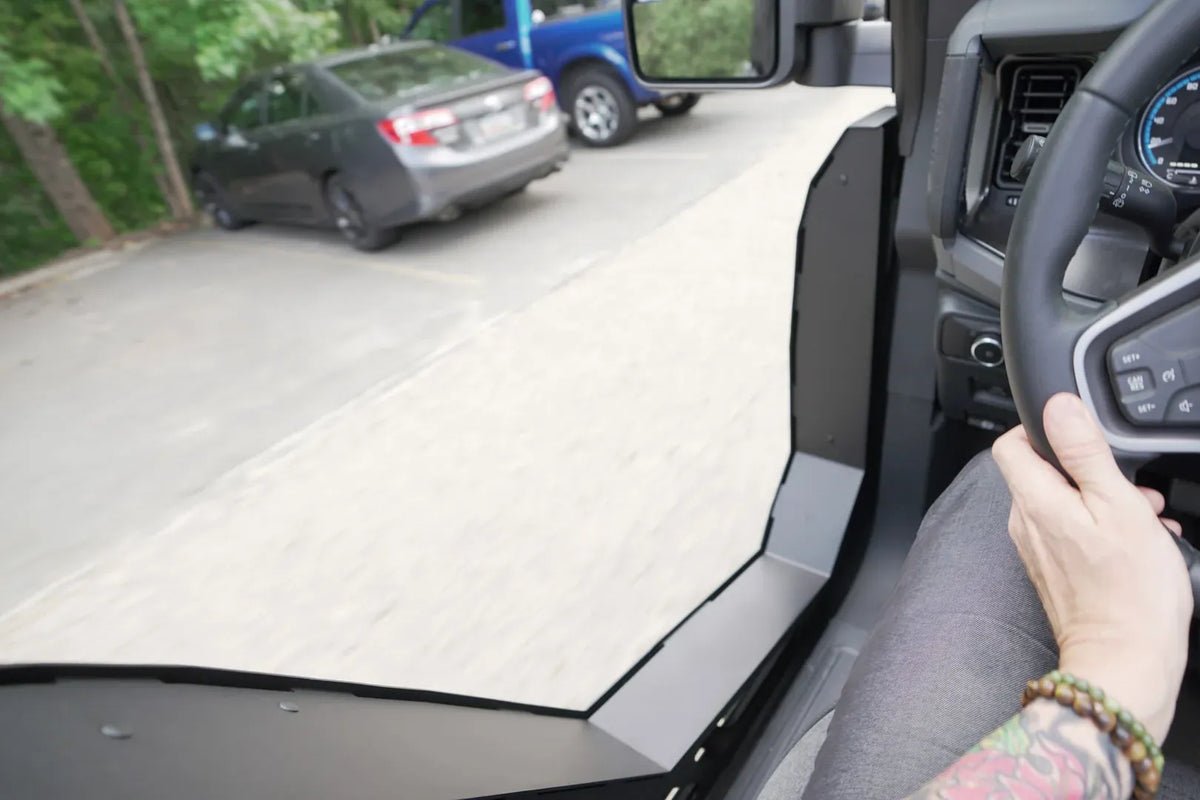Driver's view from inside a Ford Bronco with Fab Fours Trail Doors, showing the low steel door edge and open view of the road beside the steering wheel