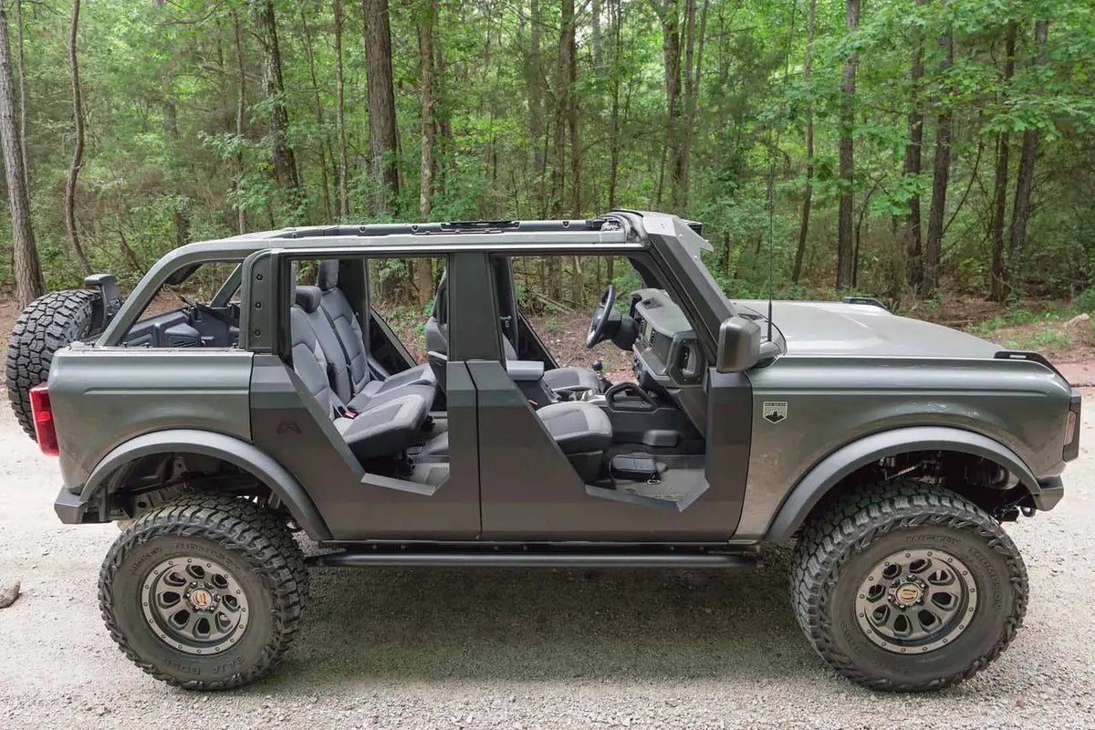Fab Fours Trail Doors on a gray four-door Ford Bronco outdoors, passenger-side profile, showing the low-cut steel doors with open views of the front and rear seats