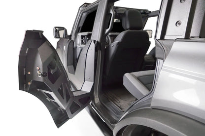 Fab Fours Trail Door swung open on the rear of a gray Ford Bronco, showing the inside of the matte black steel door with bolted hinges, latch and cutout frame