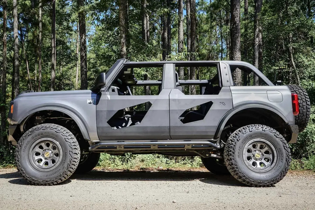 Fab Fours Trail Door Inserts on a lifted gray four-door Ford Bronco outdoors, driver-side profile, with the angular steel door inserts and Fab Fours logo on the rear door