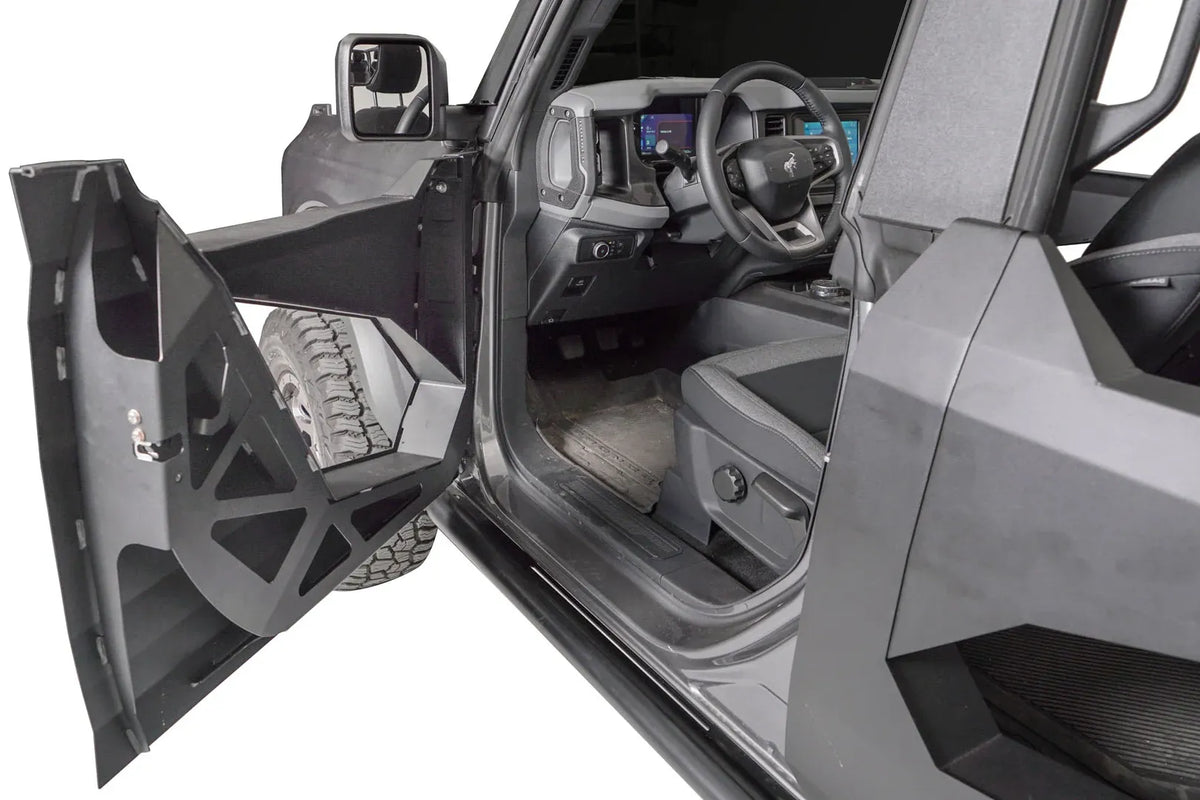 Fab Fours Trail Door Insert on an open driver-side trail door of a gray Ford Bronco, showing the matte black steel insert with angular cutouts bolted inside the door frame