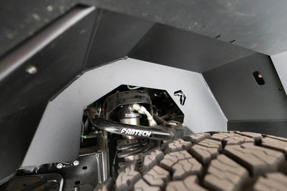 Fab Fours inner fender liner on a Ford Bronco, close-up inside the front wheel well, showing the black steel panels with the Fab Fours logo and the shock and upper control arm cut-out