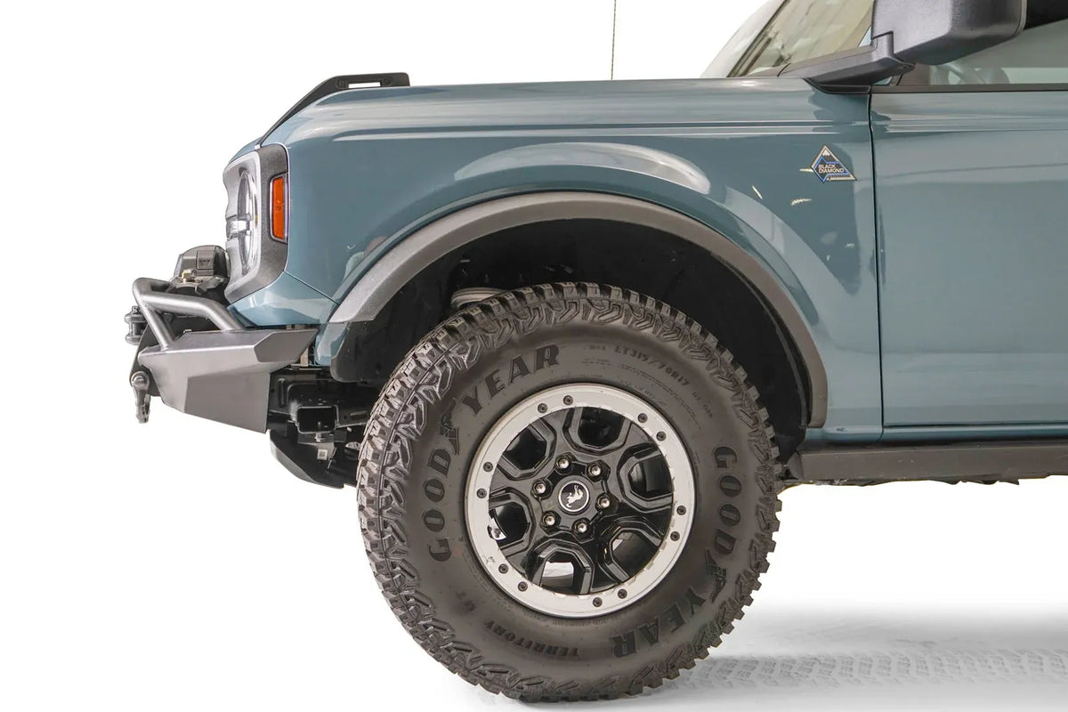 Fab Fours Stubby bumper with pre-runner guard on a blue-gray Ford Bronco, close-up of the driver-side bumper end, showing the stubby end cap, pre-runner tube and tire clearance