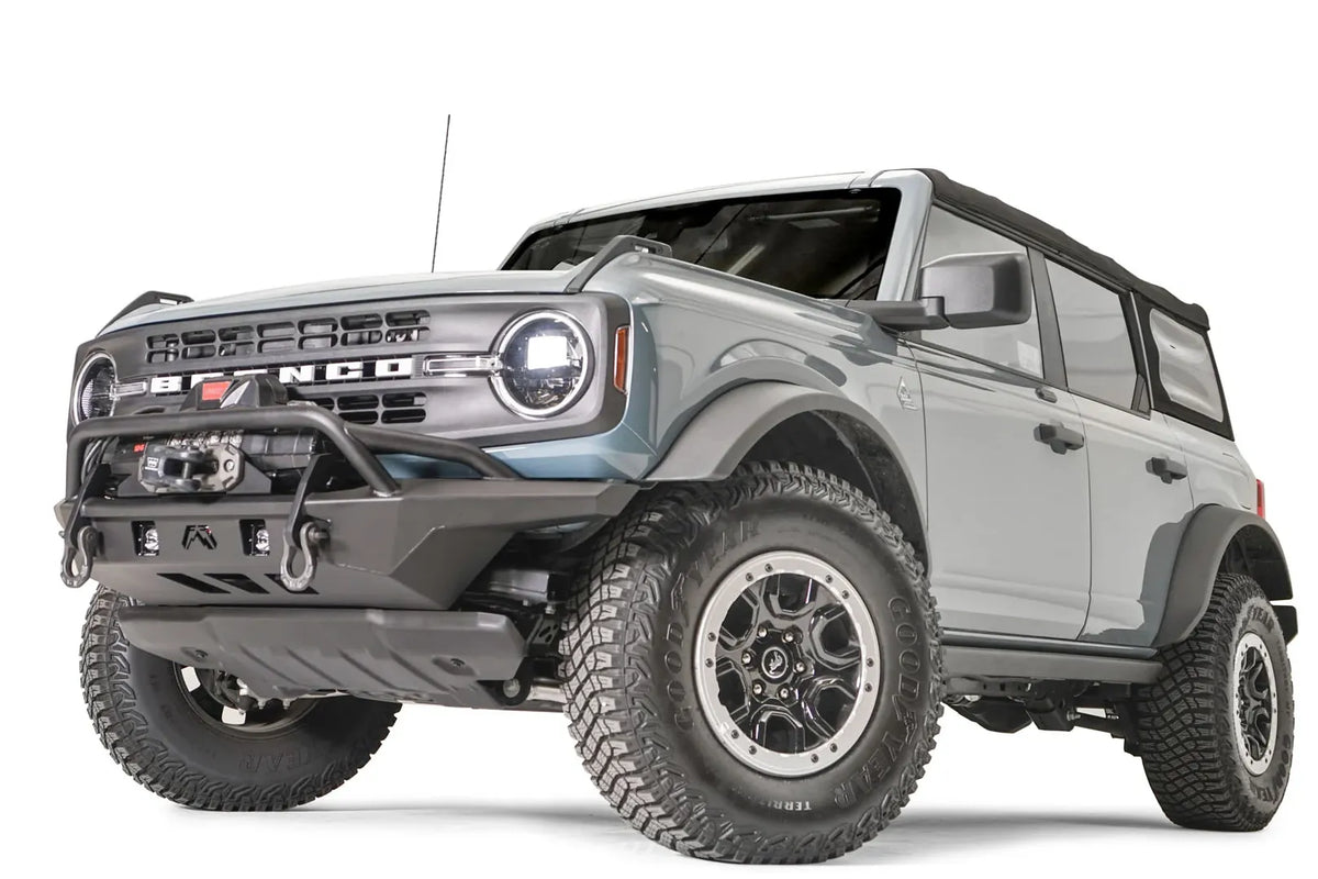 Fab Fours Stubby bumper with pre-runner guard on a light gray Ford Bronco, front driver-side three-quarter studio view, showing the pre-runner hoop, winch mount and skid plate