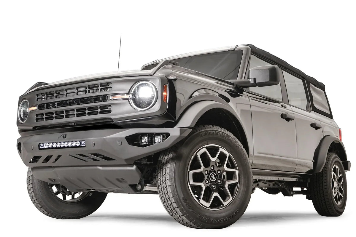 Fab Fours Vengeance front bumper on a black Ford Bronco, front driver-side three-quarter studio view, showing the low-profile bumper, light bar and skid plate