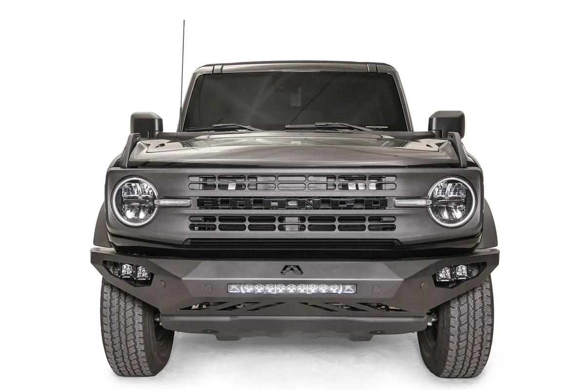 Fab Fours Vengeance front bumper on a black Ford Bronco, straight-on front studio view, showing the sculpted bumper face, center light bar and cube light pods